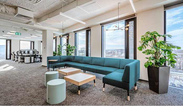 Les bureaux de Sprout Social en Pologne, avec un salon composé d'un canapé et de tables, entouré de grandes fenêtres et de plantes.​​ 