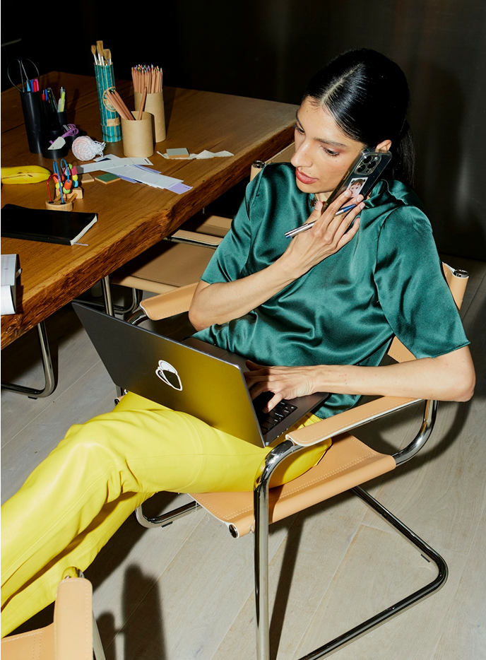 Person in a teal shirt talking on the phone while typing on their laptop, symbolizing direct communication and relationship building on social media.